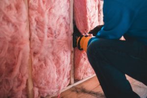 A person installing fiberglass insulation between wall studs