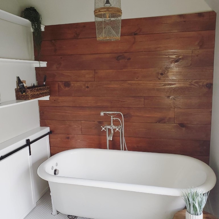 Wood look ceramic tile wall behind a white footed soaking tub.