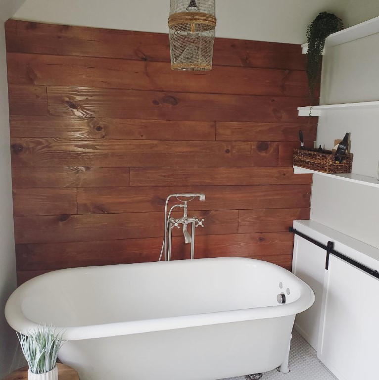 Wood look ceramic tile wall behind a white footed soaking tub.